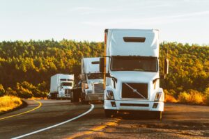 Three semi trucks driving on a highway through a forested landscape in Arizona.